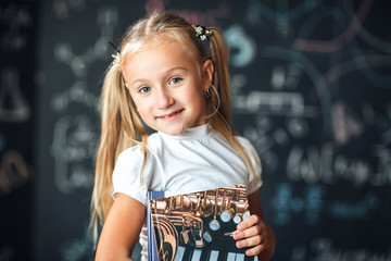 blond girl standing near a black slate with a pile of books. Free space. Black background. School concept.