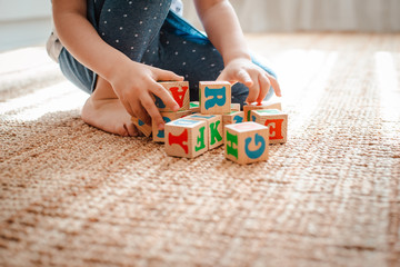 child plays with wooden blocks with letters on the floor in the room a little girl is building a tower at home or in the kindergarten.