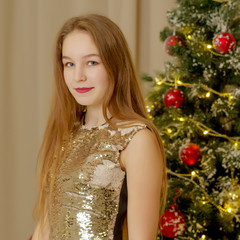 A teenage girl is sitting near the New Year tree.