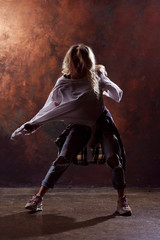 Fototapeta na wymiar Photo of young dancing blonde in ripped jeans and sneakers on dark brown background