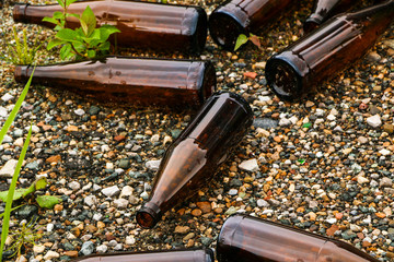 whole and broken brown bottles are scattered on gravel.Concept: waste recycling, disposal of garbage