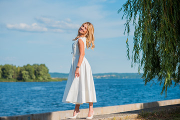 Elegant blonde hair woman in white midi dress at shore. Concept oа white code, fashionable lady,...