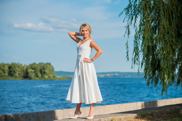Fototapeta na wymiar Elegant blonde hair woman in white midi dress at shore. Concept oа white code, fashionable lady, pretty dress and clothes 