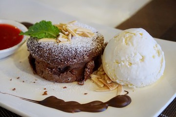 Blurred image of chocolate lava cake with vanilla ice cream and strawberry sauce in white plate on...