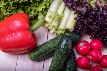 fresh vegetables on a light wooden table, paprika, celery, leaves of lettuce, cucumbers and radishes