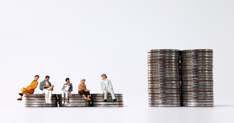 Miniature people sitting on piles of coins.