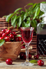 Cherry liquor and red cherries in a wooden bowl on a wooden table in garden.