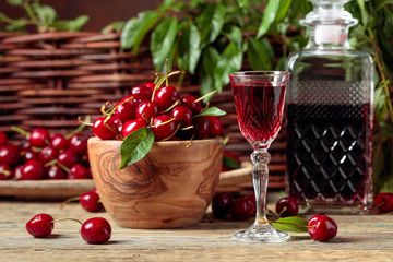 Cherry liquor and red cherries in a wooden bowl on a wooden table in garden.