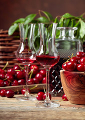 Cherry liquor and red cherries in a wooden bowl on a wooden table in garden.