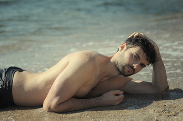 Young sexy man portrait laying in seawater, topless