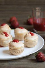 Meringue cream with fresh strawberreis in waffle cups on white plate and strawberry juice in glass on wooden background. Food photo. Front view