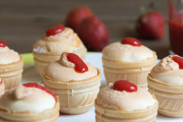 Obraz na płótnie Canvas Meringue cream with fresh strawberreis in waffle cups on white plate and wooden background. Food photo. Front view