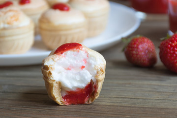 One fresh tasty meringue cream bitten off fresh strawberry in waffle cup on wooden background. Food photo. Close up. Side view