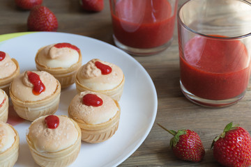 Meringue cream with fresh strawberreis in waffle cups on white plate and strawberry juice in glass on wooden background. Food photo. Front view
