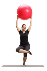 Young woman lifting a fitness ball and exercising on a mat