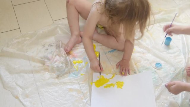 the child draws with paints and brush sitting on the floor