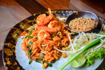 Thai food, stir fry rice noodles with shrimps, tofu, vegetable and crushed peanuts or pad thai on wooden table background, pad thai is a popular Thai street food among tourists visiting Thailand.