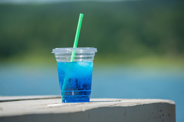 Blue drink in a plastic cup with a green straw sitting on the edge of the wooden table.