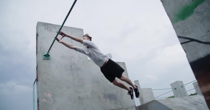 Young man does a flip from the horizontal bar, parkour on workout training area, free running in slow motion.