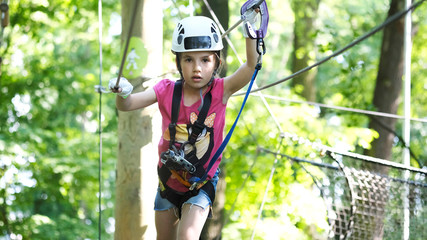 Cute preschool girl in climbing gear in a rope park, family outdoor activities, happy summer time, sports and an active lifestyle