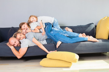Whole family of five lying on top of each other in the living room.The father lies across the couch...