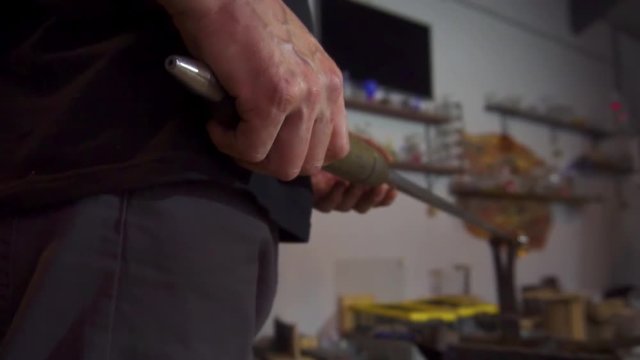 Glassblower in his workshop taking out rod with liquid glass and rotating it. Close-up.