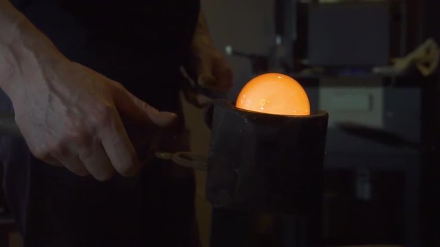 Glassblower in his workshop and rotating rod with liquid glass. Close-up.