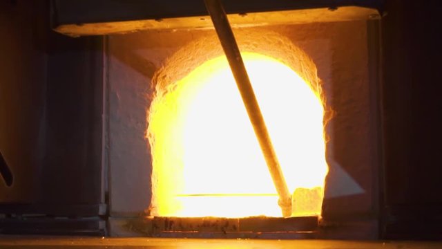 Glassblower in his workshop taking out rod with liquid glass and rotating it. Close-up.