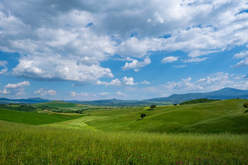 Fototapeta premium Picturesque Tuscany landscape with rolling hills, valleys, sunny fields, cypress trees along winding rural road, houses on a hill. Tourist visit in Tuscany