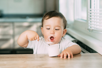 A little charming girl eats yogurt all smeared herself