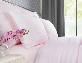 Bed with pink bed linen against a window with grey curtains.