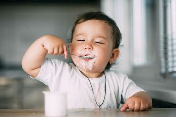 A little charming girl eats yogurt all smeared herself