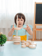 little girl collects a wooden unpainted pyramid. Safe natural wooden children's toys.
