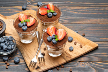 Classic tiramisu dessert with blueberries and strawberries in a glass on wooden background