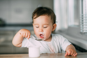 A little charming girl eats yogurt all smeared herself