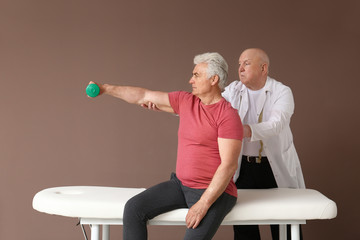 Obraz premium Senior physiotherapist working with mature man on color background
