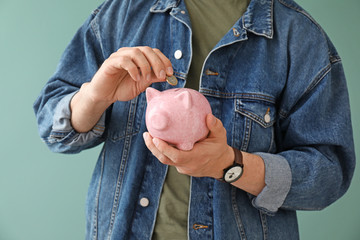 Young man with piggy bank on color background, closeup