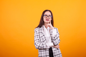Cute caucasian girl with eyeglasses looking up and thoughtful over yellow background