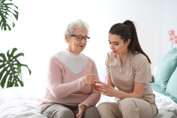 Caregiver giving medicine to senior woman in nursing home