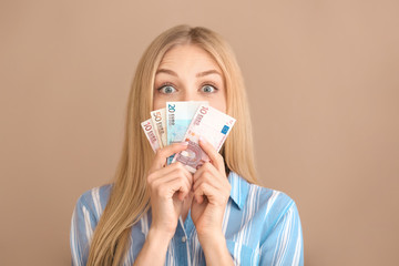 Surprised young woman with money on color background