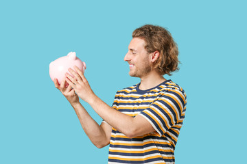 Handsome man with piggy bank on color background