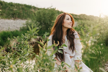 Beautiful carefree long hair asian girl in white clothes on river side in grass at sunset. Sensitivity to nature concept