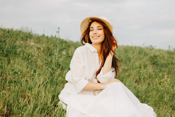 Charming carefree long hair asian girl in white clothes and straw hat enjoys life in the field at sunset. Sensitivity to nature concept