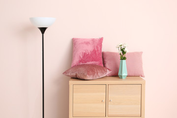 Cabinet with soft pillows and lamp near color wall