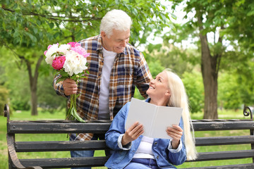 Fototapeta premium Mature woman receiving flowers from her husband in park