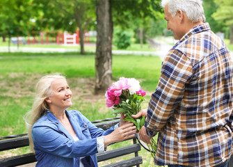 Mature woman receiving flowers from her husband in park