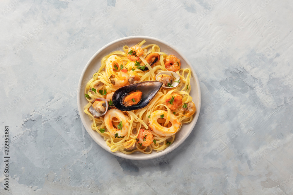 Wall mural Seafood pasta. A plate of tagliolini with mussels, shrimps, clams and calamari rings, shot from the top with copy space