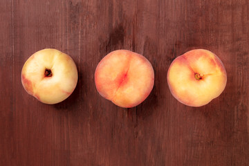 Vibrant organic flat saturn peaches, shot from above on a dark rustic wooden background with a place for text
