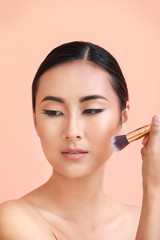 Asian woman with beautiful makeup and brush on color background