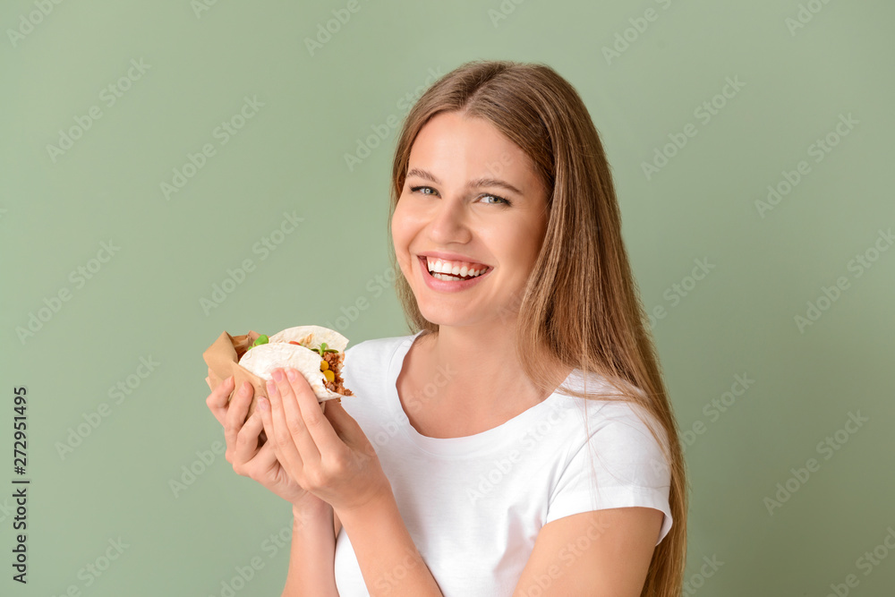 Wall mural woman eating tasty taco on color background